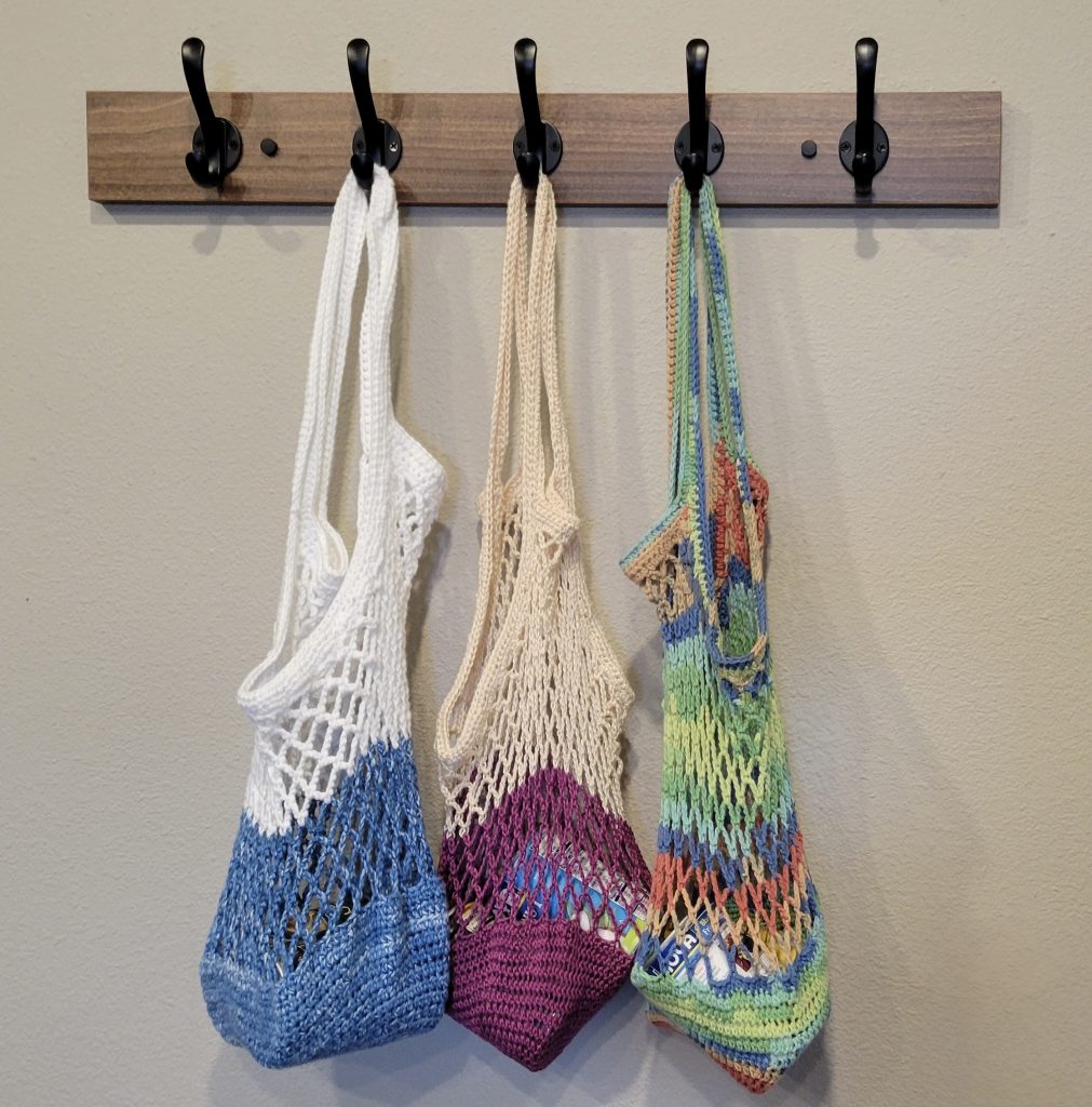 Three colorful market bags hanging on coat rack hooks.